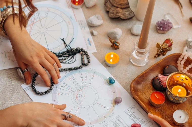 Hands arranging astrology charts with candles and crystals on a table for a spiritual ritual.